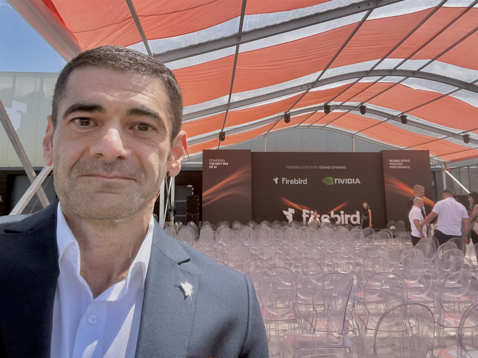 The author in front of the event stage under an orange and white canopy, with rows of empty chairs before the ceremony.